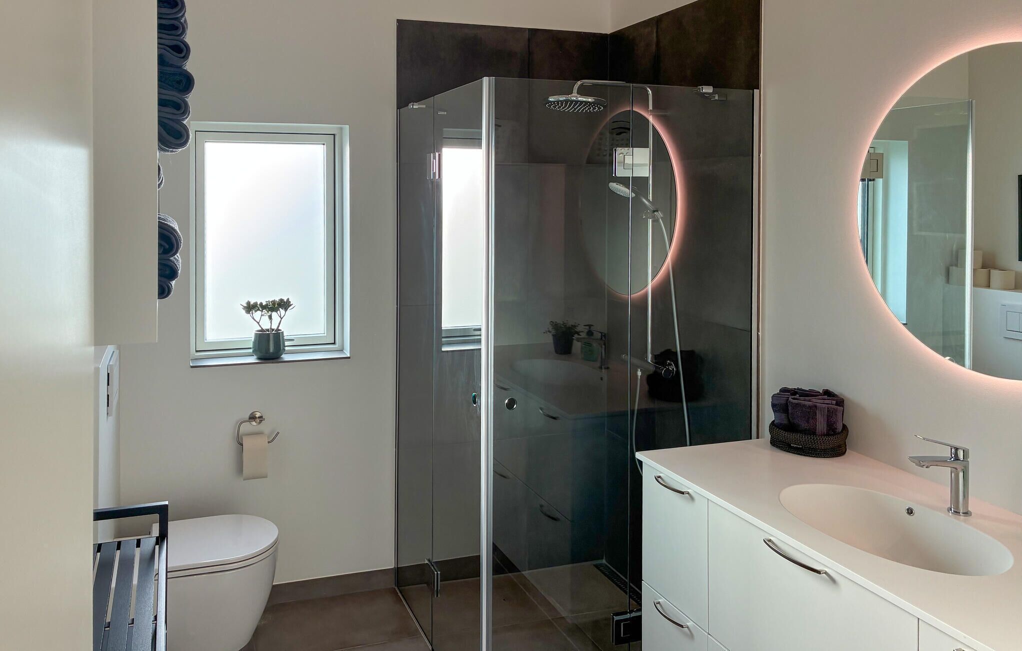 A modern bathroom with a glass-enclosed shower, a white sink, and a large mirror.