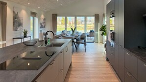 Una cocina moderna con una isla central, ventanas amplias y un comedor con mobiliario exterior.