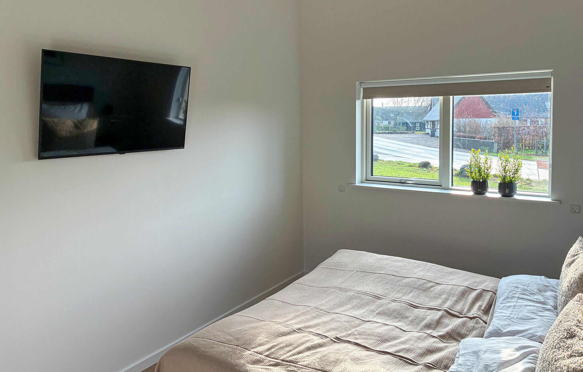 Een slaapkamer met een bed, een aan de muur bevestigde televisie en een raam met uitzicht.