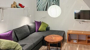 Moderni olohuone, jossa on harmaa kulmasohva, pieni puinen sohvapöytä ja televisio valkoisella seinällä.