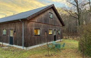 A rustic wooden barn with a sloped roof, multiple windows, and a small outdoor seating area with chairs. - Gorgeous home in Faxe with WiFi (Faxe)
