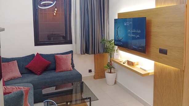 Ein stilvolles Wohnzimmer mit Sofa, Couchtisch, Wandfernseher und einer Topfpflanze.