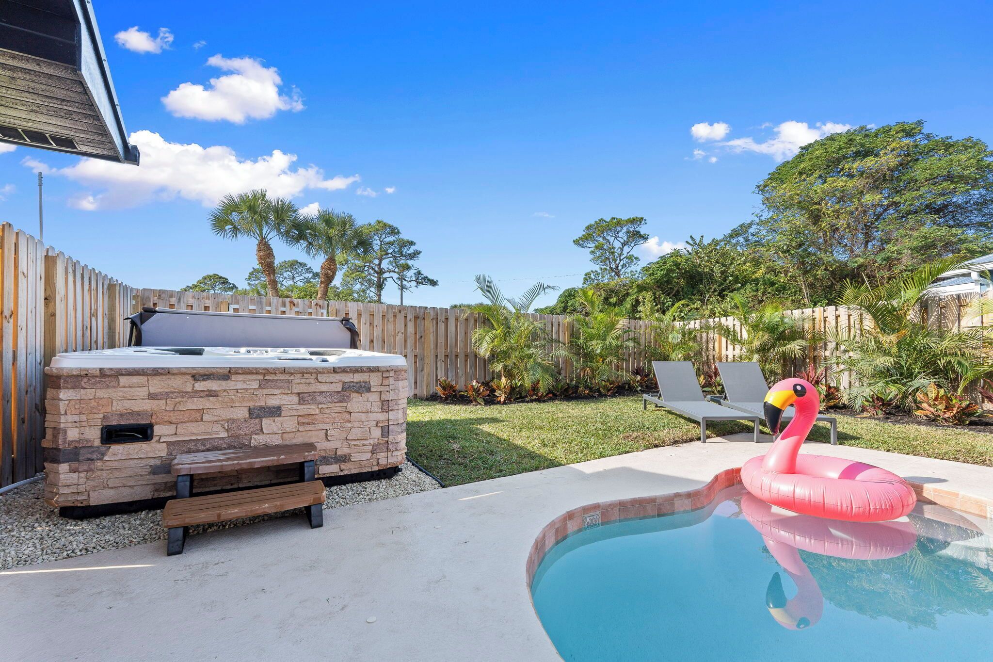A backyard with a hot tub, a pool, and a flamingo float.