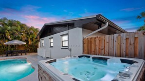 Una casa moderna con idromassaggio e piscina, circondata da una recinzione in legno e palme.