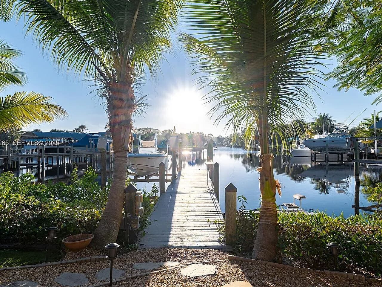 A wooden dock leading to a marina with boats and a clear sky.