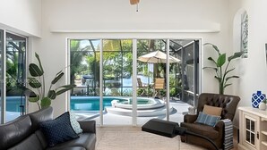 Ein modernes Wohnzimmer mit Ledersofa, Couchtisch und einer großen Schiebeglastür zum Poolbereich.