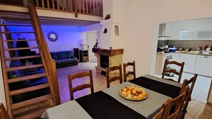 A dining area with a table set for four, a wooden staircase, and a kitchen in the background.