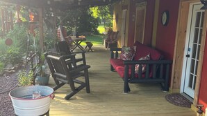 A covered outdoor patio with wooden flooring, a metal bucket, and a rocking chair.