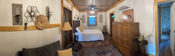 A narrow hallway leading to a bedroom with a bed, a wooden wardrobe, and a small table.