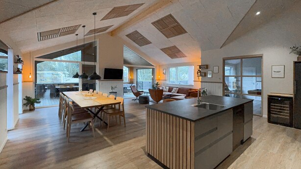 Een ruime keuken met een centraal eiland, grote ramen en een eethoek met een lange tafel en stoelen.