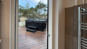 Een houten terras met jacuzzi's en een bankje, dat uitkomt op een bebost gebied.