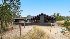 Een moderne blokhut met een groot raam, gelegen in een natuurrijk landschap en voorzien van een schommel.