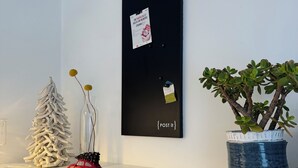 Un rellotge penjat a la paret amb disseny minimalista, una petita planta en test i alguns objectes decoratius sobre una prestatgeria blanca.