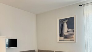 Una habitació amb un llit, una televisió penjada a la paret i un quadre sobre el llit.