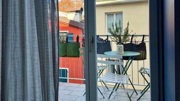 Vista d'una habitació amb porta corredissa de vidre a un patí exterior. El patí té una taula rodona amb cadires i una petita planta en test.