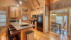 A wooden cabin kitchen with granite countertops, a black refrigerator, and a dining area with a table and chairs. - Black Bear Ridge (Blairsville)