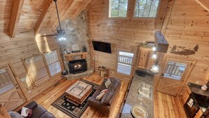 A cozy cabin interior with a stone fireplace, wooden walls, a sofa, and a kitchen area. - Black Bear Ridge (Blairsville)