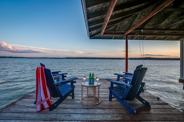 A wooden deck with blue chairs and a small table with bottles and glasses.