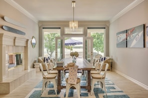 A dining room with a long table, chairs, a chandelier, a fireplace, and large windows.