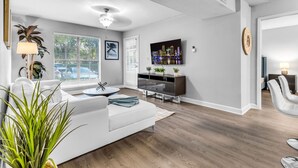 A modern living room with a white sofa, a glass coffee table, a TV, and a fireplace. - Walk to Las Olas + 15 Min to Beach + Sleeps 6 (Fort Lauderdale)