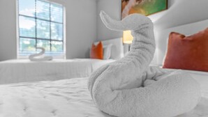 A white, plush, swan-shaped towel on a bed in a hotel room with a large window, a painting on the wall, and a red pillow. - Walk to Las Olas + 15 Min to Beach + Sleeps 6 (Fort Lauderdale)