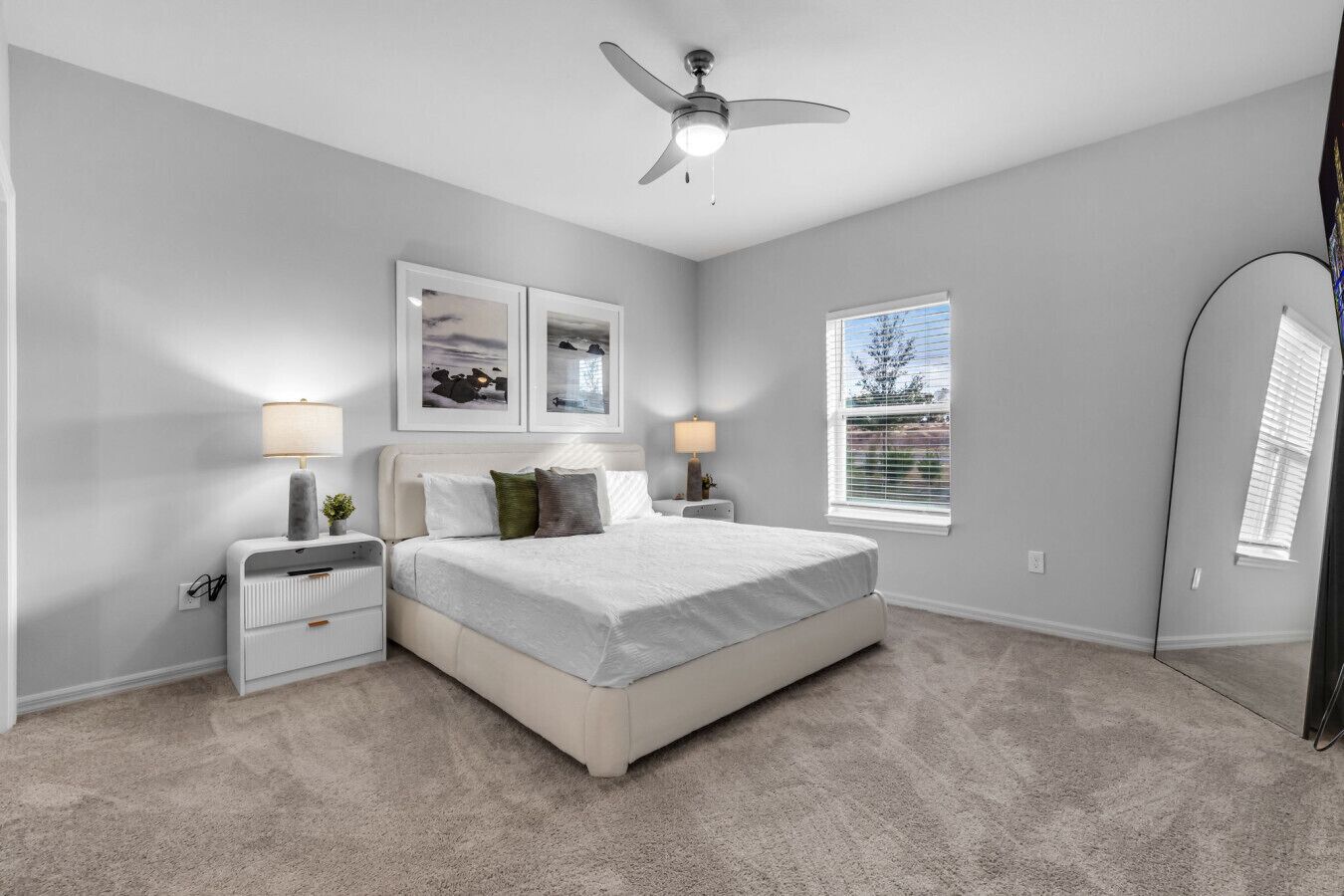 A bedroom with a bed, two bedside tables, a ceiling fan, and a window with blinds.