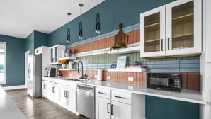 Una cocina moderna con armarios blancos, un refrigerador de acero inoxidable, un lavavajillas y un microondas.