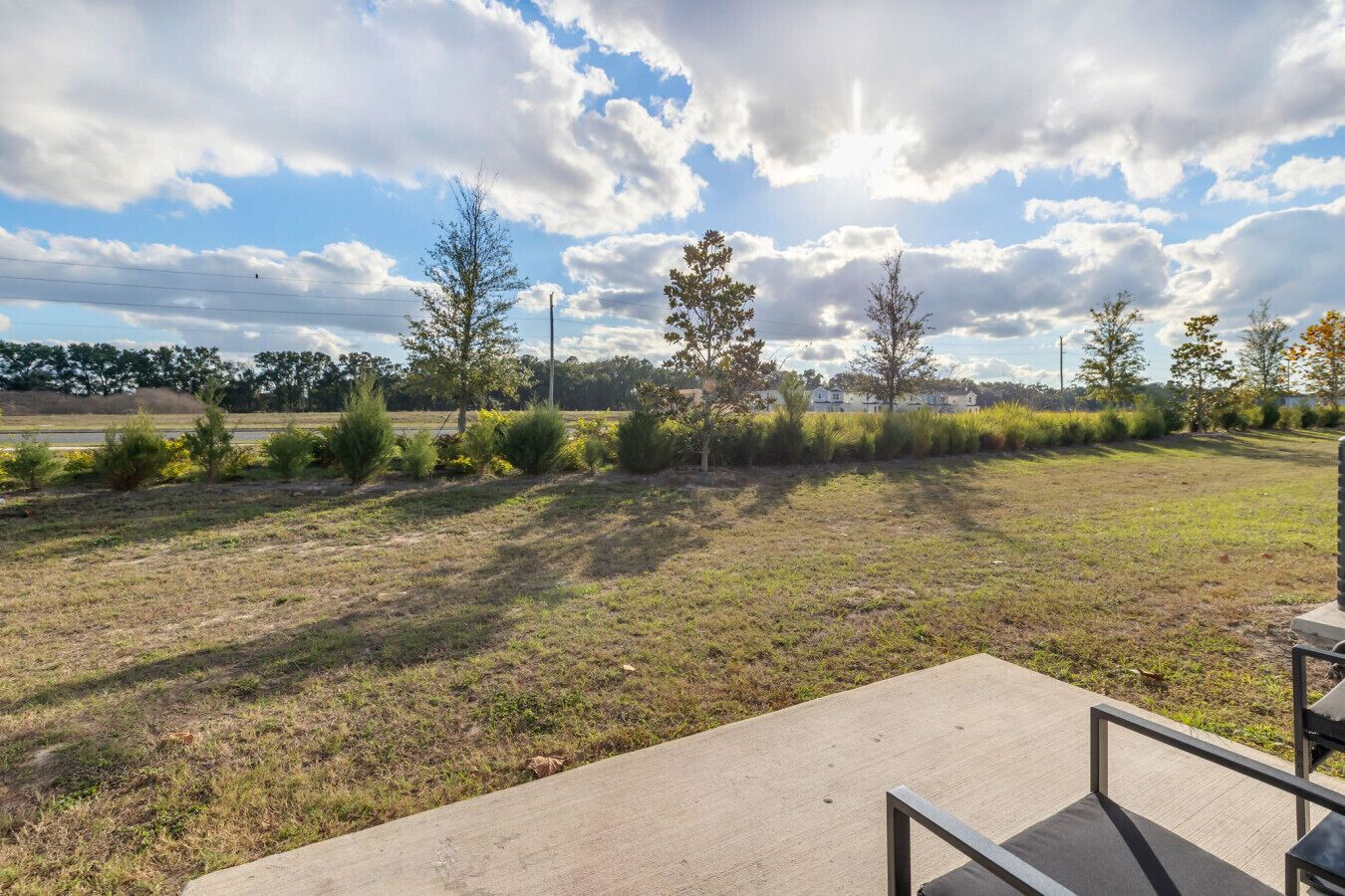 An outdoor area with a concrete pathway, small trees, and a grassy field.