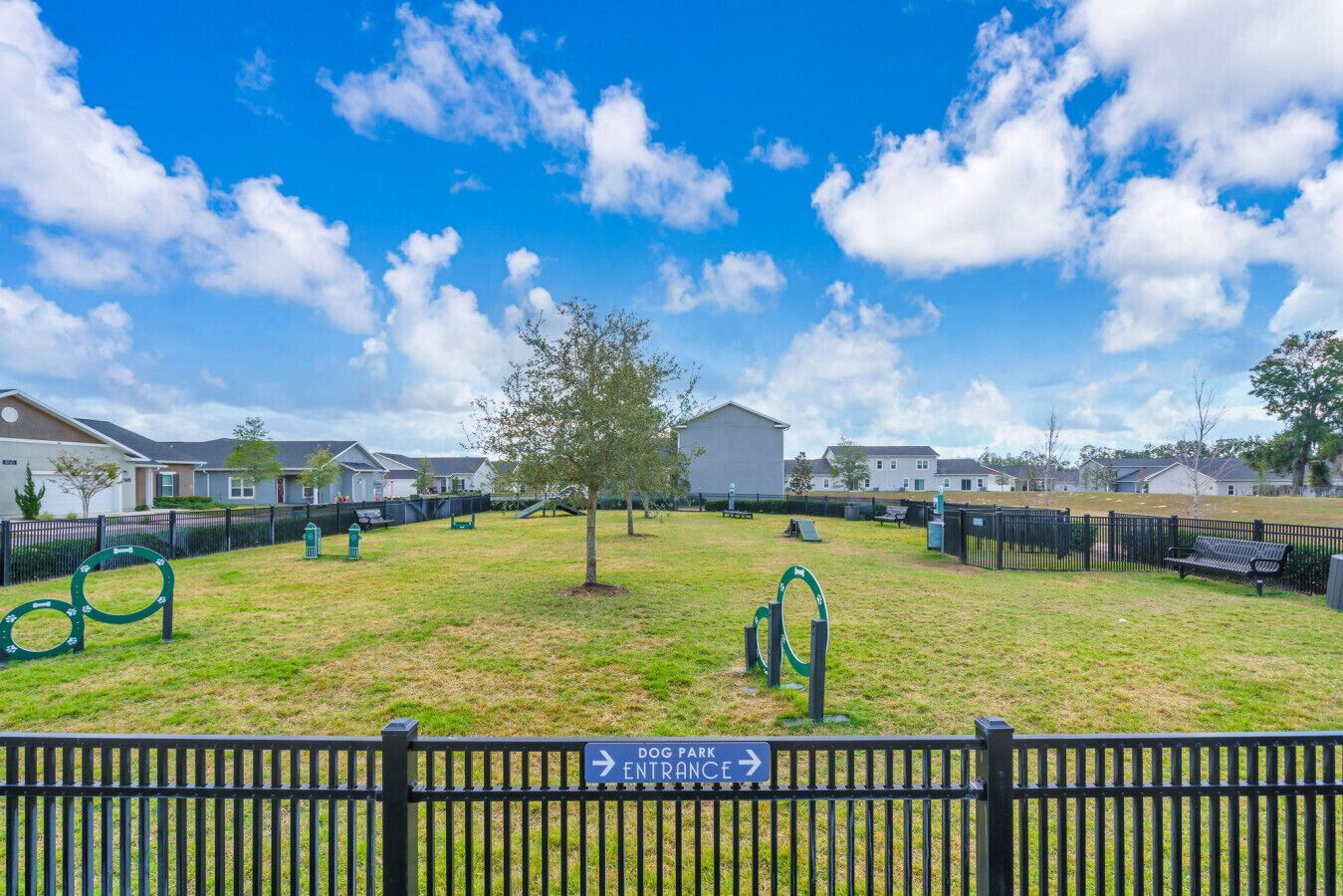 A fenced dog park with a sign indicating the entrance direction.