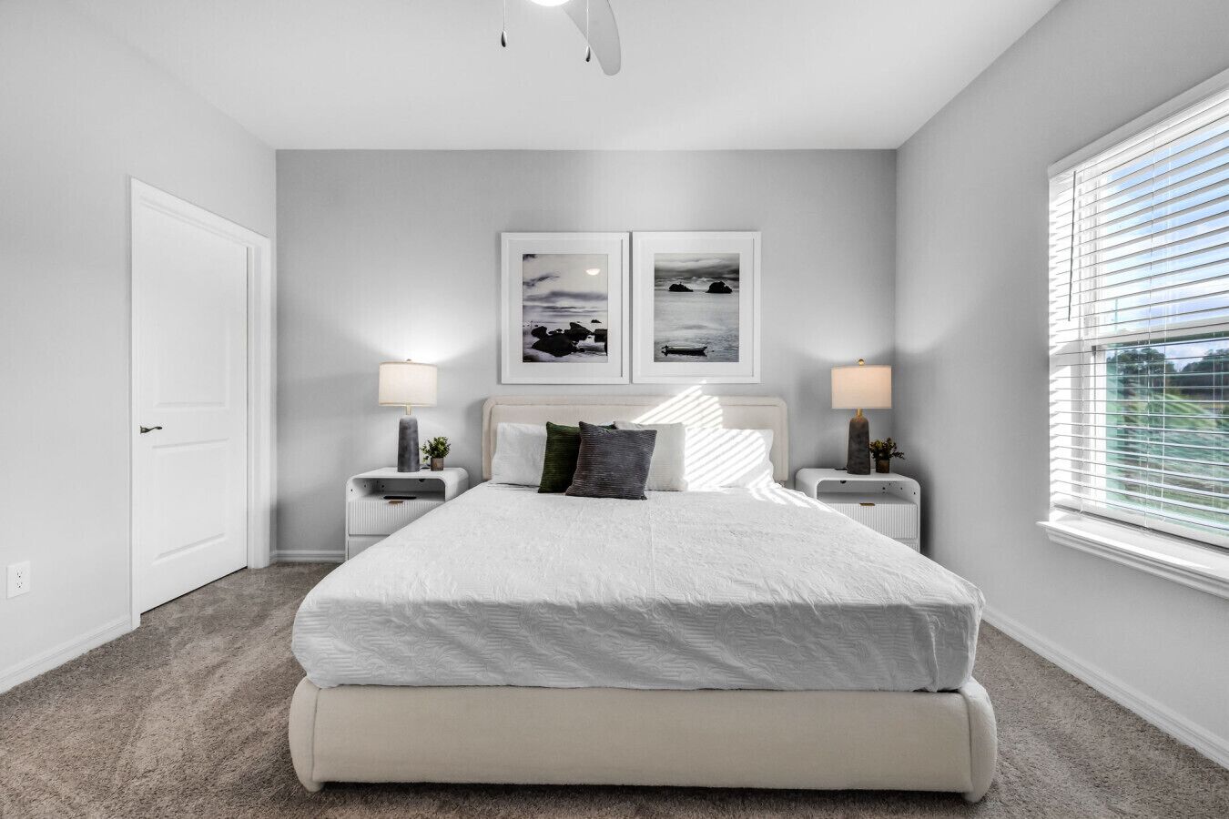 A bedroom with a large bed, two bedside tables, a door, and a window with blinds.