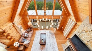 Ein gemütliches Holzinterieur mit Schlafzimmer im oberen Bereich, einem Kamin aus Stein und Blick auf die Berge.