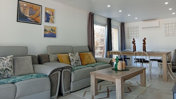 Una sala moderna con un sofá gris, una mesa de centro de madera y una zona de comedor con una mesa y sillas de madera.