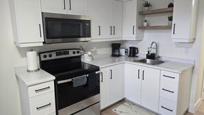 A compact kitchen with white cabinets, a black stove, a microwave, a coffee maker, and a sink.