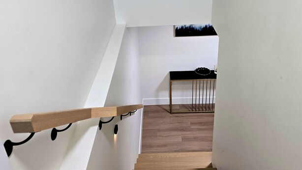 A staircase with wooden steps and white walls, leading to a landing with a small table and a chair.