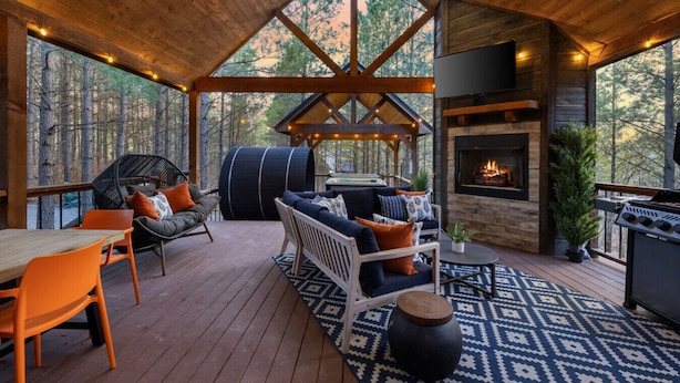 Eine Holzterrasse mit Sitzgelegenheiten im Freien, einem Kamin und Blick auf den Wald.