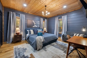 Ein Schlafzimmer mit einem großen Bett, einer Holzbalkendecke und Blick ins Freie durch ein Fenster.