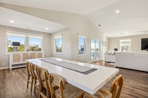 A spacious living area with a dining table, chairs, a sofa, and a TV. - KH112 Sound Decision by First Flight Rentals (Kitty Hawk)