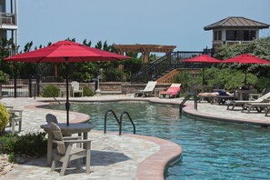 Ein Poolbereich mit roten Sonnenschirmen, Liegestühlen und einer Terrasse mit Steinfliesen.