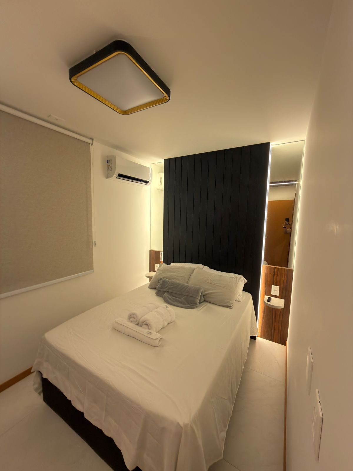 Une chambre d’hôtel moderne avec un lit bien fait, une table de chevet avec une lampe et une tête de lit sombre.