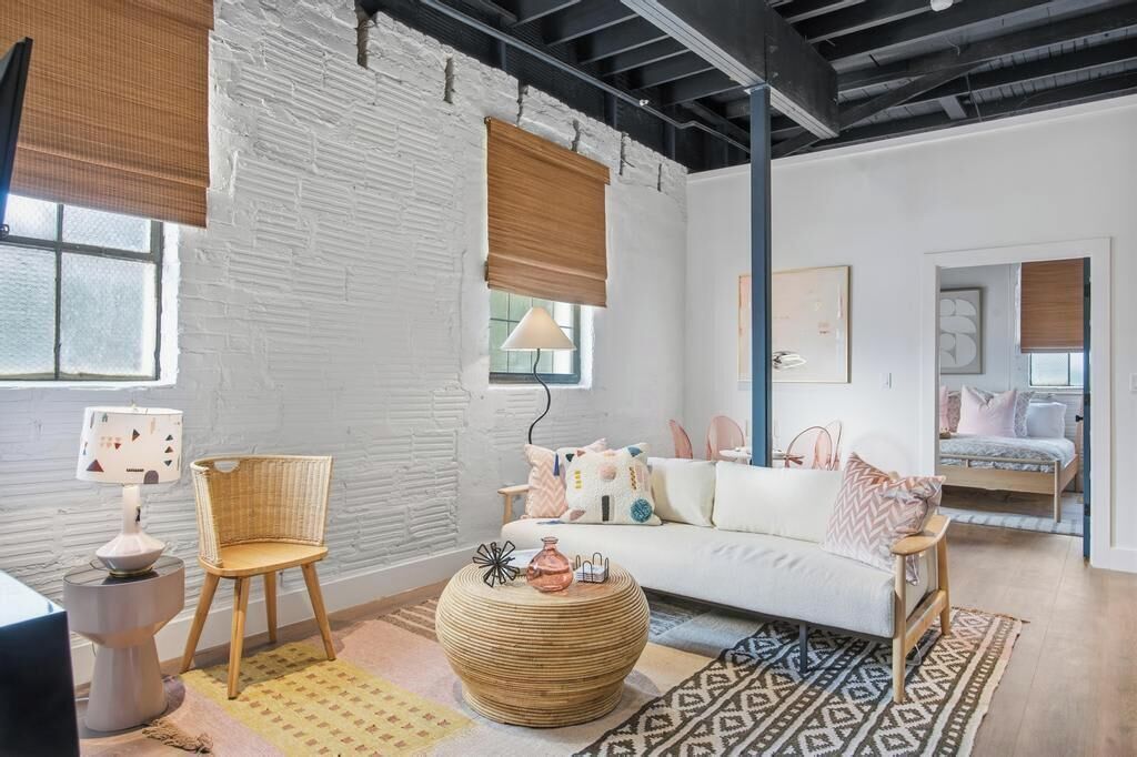 Un salon moderne avec un mur en briques blanches, un canapé blanc, une table basse ronde en bois et un fauteuil en osier.