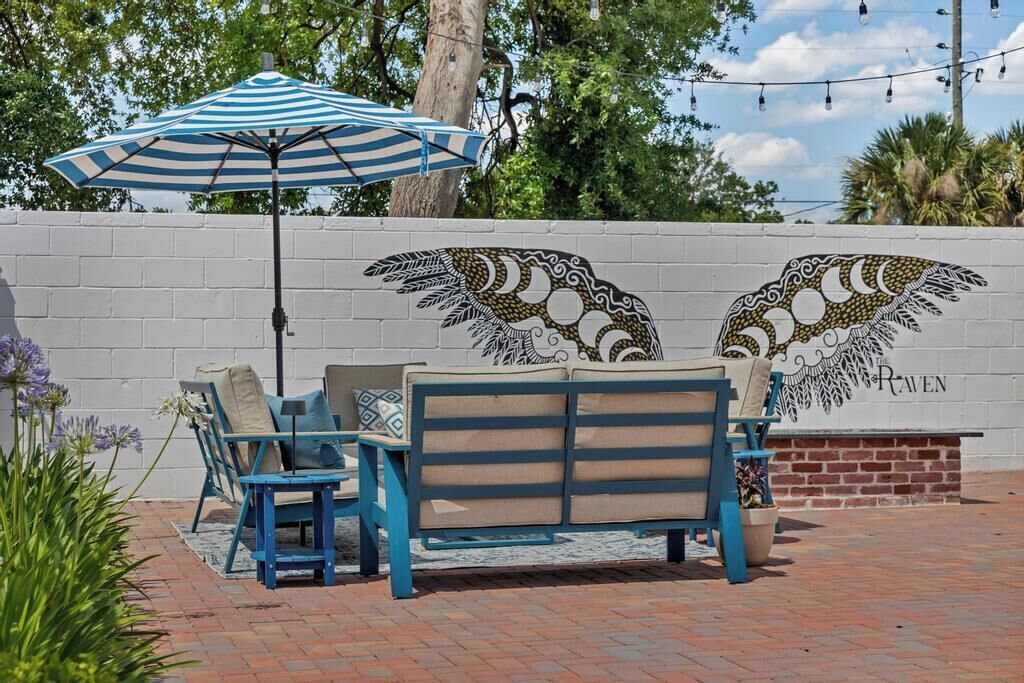 Une terrasse agrémentée d’un parasol à rayures bleues et blanches, d’un canapé bleu et d’une fresque murale représentant un motif d’oiseau.