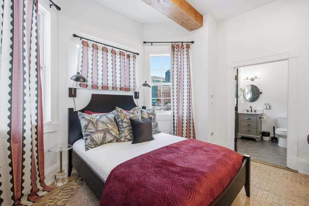 A bedroom with a bed, a nightstand, a mirror, and a view of the city.