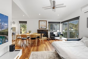 A modern bedroom with a bed, a fireplace, a dining area with chairs, and large windows.
