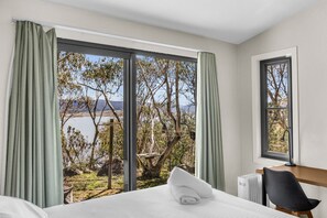 A bedroom with a large window, a bed, a chair, and a radiator. - Lakeview Lodge | East Jindabyne | Lakefront | 3BR (East Jindabyne)