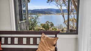 Un banco de madera con cojín, una ventana con vistas a un lago y montañas, y una pared blanca.