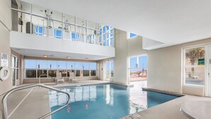 Une piscine intérieure dotée d’une balustrade en verre, de chaises longues et offrant une vue sur l’extérieur.