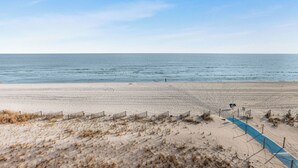 Une plage avec un rivage sablonneux, une personne qui se promène et un chemin bleu.