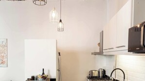 Een kleine keuken met een bakstenen plafond, witte kasten, een zwart aanrecht en hangende pendantlampen.