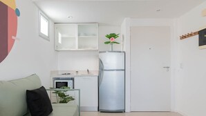 Un espace de vie compact comprenant un coin cuisine, un canapé avec des coussins, un réfrigérateur et une porte.