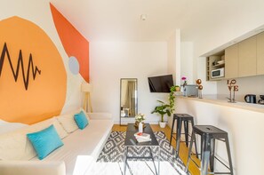 Ein modernes Wohnzimmer mit Sofa, Couchtisch und einer Küchenzeile inklusive Mikrowelle und Schränken.